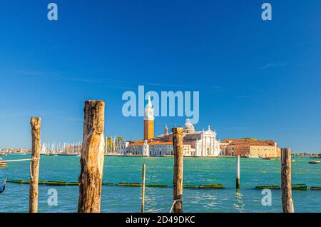 Insel San Giorgio Maggiore mit Campanile San Giorgio in der Lagune von Venedig, Holzmasten im Wasser des San Marco-Beckens im Vordergrund, blauer klarer Himmel, Region Venetien, Italien, Stadtbild von Venedig Stockfoto