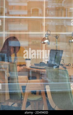 Kasan, Russland, 16. September 2020. Eine junge Frau sitzt an einem Laptop in der Bibliothek. Seitenansicht durch Fensterglas Stockfoto