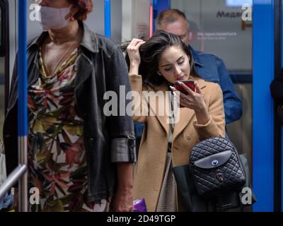 Moskau. Russland. September 25, 2020. Ein junges dunkelhaariges Mädchen steht mit einem Smartphone in der Hand in einem U-Bahn-Auto und passt die Haare an. Das Mädchen Stockfoto