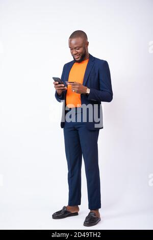 Junger afrikanischer Geschäftsmann, der sein Telefon und seine Kreditkarte benutzt und vor einem weißen Hintergrund steht Stockfoto