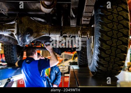 Riga, Lettland - 12 April 2019: ein Mechaniker prüft die technischen Stand unter einem angehobenen Auto auf einer Brücke in einer Garage - Bild Stockfoto