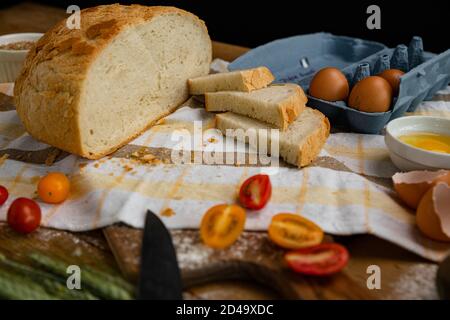 Frisches Brot zusammen mit Tomaten und Eiern auf ein Handtuch gelegt. Bäckerei - Gold rustikale knusprige Brote. Stillleben von oben (Draufsicht, Stockfoto
