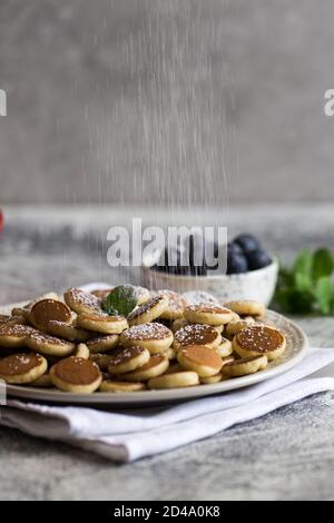 Zum Frühstück gab es winzige Pfannkuchen. Cereal Pancakes mit Heidelbeeren in Teller auf grauem Hintergrund. Trendiges Essen. Platz für Text oder Design kopieren Stockfoto