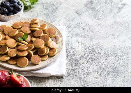 Zum Frühstück gab es winzige Pfannkuchen. Cereal Pancakes mit Heidelbeeren, Bananen, Erdbeeren auf grauem Hintergrund. Trendiges Essen. Platz für Text oder Design kopieren Stockfoto