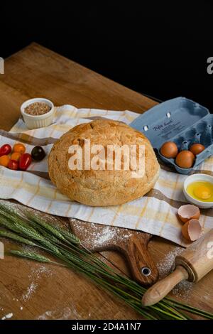 Frisches Brot zusammen mit Tomaten und Eiern auf ein Handtuch gelegt. Bäckerei - Gold rustikale knusprige Brote. Stillleben von oben (Draufsicht, Stockfoto