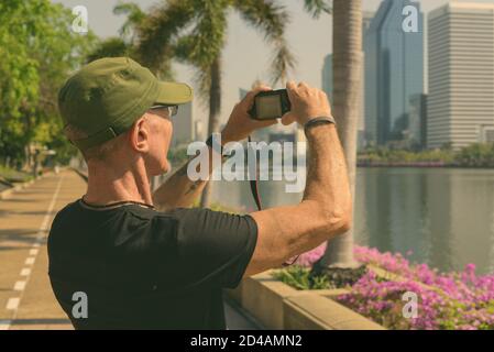 Senior touristische Mann mit Kappe während Bilder im ruhigen Park in Bangkok, Thailand, Stockfoto