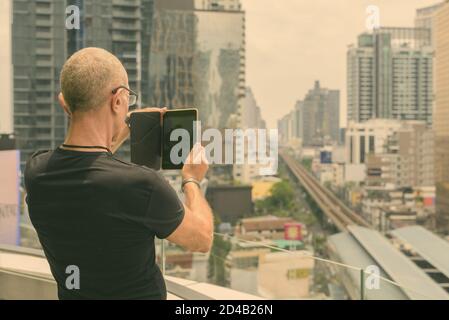 Rückansicht des kahlen Senior touristische Mann mit digitalen Tablet die Ansicht der Stadt in Bangkok, Thailand Stockfoto