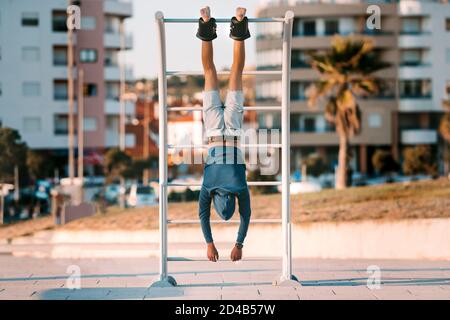 Mann, der kopfüber an der horizontalen Stange in Anti-Schwerkraft- oder Inversionsstiefeln hängt. Sportausrüstung. Gesunder Lebensstil. Stockfoto