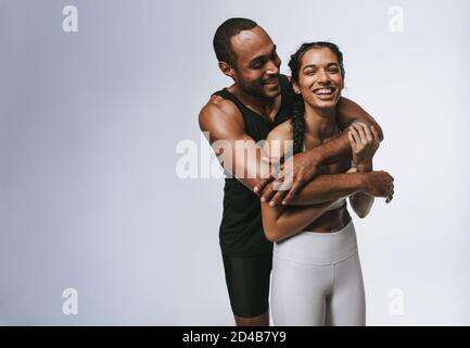 Fröhliche Athleten, Männer und Frauen, die zusammen stehen und Spaß haben. Fitness-Mann hält weibliche Athletin nach dem Training in den Armen. Stockfoto