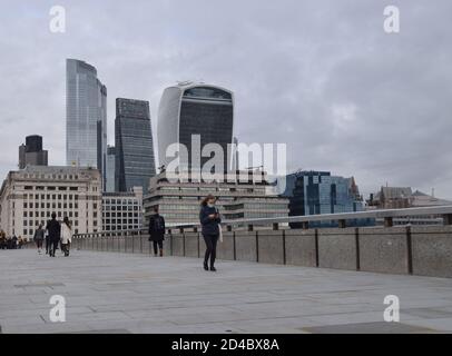 Eine Frau mit einer schützenden Gesichtsmaske geht über die London Bridge mit City of London im Hintergrund, London, UK 2020 Stockfoto