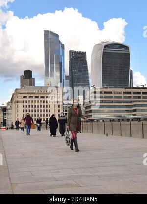 Eine Frau mit einer schützenden Gesichtsmaske geht über die London Bridge mit City of London im Hintergrund, London, UK 2020 Stockfoto