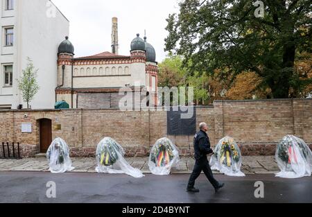 09. Oktober 2020, Sachsen-Anhalt, Halle (Saale): Ein Polizist geht an den Kränzen des Gedenktages vorbei, noch in Folie gehüllt, vor der Synagoge. Ein Jahr nach dem rechtsgerichteten Terroranschlag auf Jom Kippur, dem höchsten jüdischen Feiertag, werden die Opfer mit Veranstaltungen und Gebeten gedenkt. Am 9. Oktober 2019 hatte ein schwer bewaffneter Rechtsextremist versucht, die Synagoge zu stürmen und unter 52 Besuchern ein Massaker zu verursachen. Als er dies nicht tat, schoss er einen Passanten und in einem Kebab beißen einen jungen Mann. Foto: Jan Woitas/dpa-Zentralbild/ZB Stockfoto