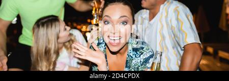 Panoramaaufnahme einer jungen Frau, die während ihrer Freunde die Kamera anschaut Toasten mit Bier in der Nacht Stockfoto