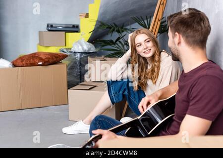 Zufrieden Frau Blick auf Mann spielen akustische Gitarre in der Nähe von Boxen, Relocation-Konzept Stockfoto
