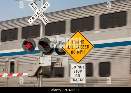 Schnellzug Warnschild am Bahnübergang mit Bewegungsunschärfe des Zuges im Hintergrund. Konzept der Sicherheit, Gefahr und Transport von Bahnübergängen Stockfoto