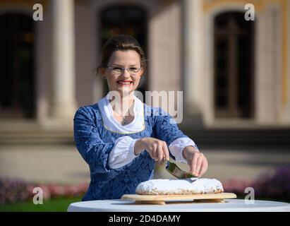 Dresden, Deutschland. Okt. 2020. Johanna Meitzner, das 26. Dresdner Stollenmädchen, schneidet den einen Weihnachtsstollen während ihres Aufführens im Schlosspark Pillnitz. Der 21-jährige Bäckerlehrling ist für ein Jahr Botschafter des Dresdner Christstollens im Auftrag der Dresdner Stollenbäcker. Quelle: Robert Michael/dpa-Zentralbild/ZB/dpa/Alamy Live News Stockfoto