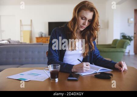 Frau, die sich Notizen machte, während sie zu Hause auf ihrem Schreibtisch saß Stockfoto