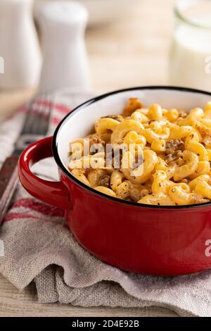 Schüssel mit Makkaroni und Cheddar-Käse mit Speckstücken und Glas Milch im Hintergrund auf einem Holztisch. Nahaufnahme Stockfoto