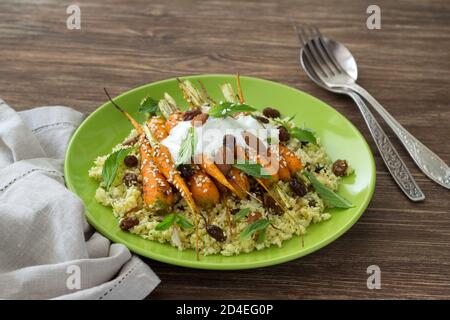 Köstlicher gesunder Blumenkohl Couscous mit gebackenen Babykarotten, Joghurt, Sesam, Nüssen, Rosinen und Minze auf einem Keramikplatte auf einem Holztisch Stockfoto
