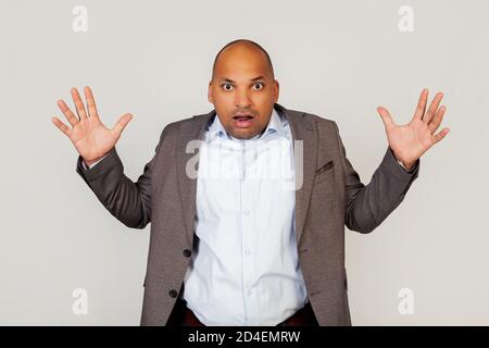 Verärgert Mann afroamerikanischen Geschäftsmann in einer Jacke, macht eine unzufrieden Geste, breitet seine Arme und schreit wild, wütend und wütend emotional hob seine Handflächen nach oben und schreit heiß in die Kamera. Stockfoto