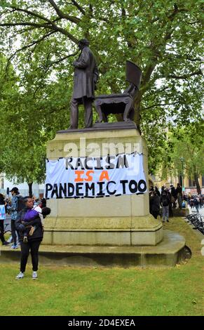 Eine Frau, die ihr Kind hält, steht vor einem Rassismus ist EIN Pandemie-Too-Banner beim Anti-Rassismus-Protest in London, 06/06/2020. Demonstranten versammelten sich auf dem Parliament Square nach dem Tod von George Floyd. Stockfoto