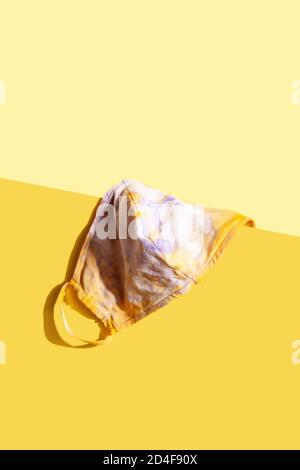 Tie-dye Textil-Schutz Gesichtsmaske auf gelbem Hintergrund. Pandemie- oder Epidemien-Konzept. Modernes Stillleben Stockfoto