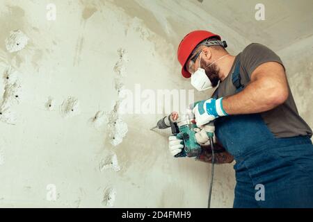 baumeister mit Perforator bohrt Löcher in Betonwand der Baumeister Ist in Schutzanzug und Helm gekleidet Stockfoto