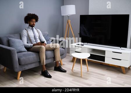 Junger Mann Sitzt Auf Der Couch Mit Smartphone Zu Hause Stockfoto