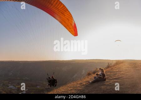 Sitzen auf einem Canyon, Blick auf Gleitschirme fliegen in den Himmel bei Sonnenuntergang. Reise mit Haustieren. Junge Familie mit einem schnauzer Hund reisen. Moldawien, Old Orhey Stockfoto