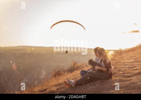 Sitzen auf einem Canyon, Blick auf Gleitschirme fliegen in den Himmel bei Sonnenuntergang. Reise mit Haustieren. Junge Familie mit einem schnauzer Hund reisen. Moldawien, Old Orhey Stockfoto