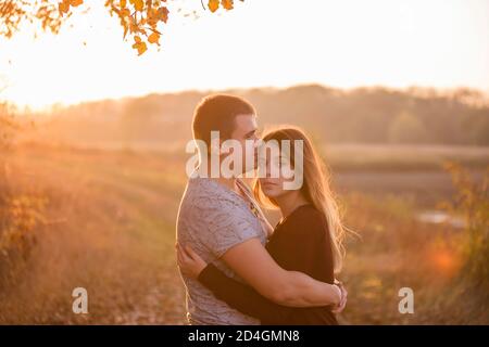 Ein junger Mann küsst, umarmt eine schöne lächelnde blonde Frau mit langen Haaren. Nahaufnahme eines Paares, das sich vor dem Hintergrund des Herbstes umarmt Stockfoto