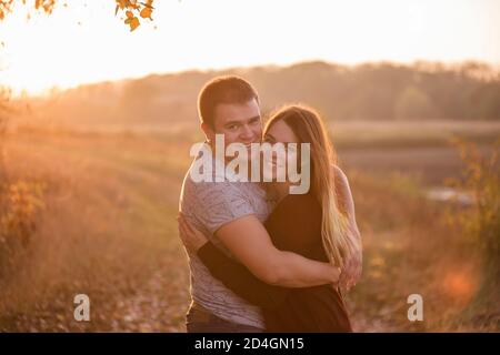 Ein junger Mann küsst, umarmt eine schöne lächelnde blonde Frau mit langen Haaren. Nahaufnahme eines Paares, das sich vor dem Hintergrund des Herbstes umarmt Stockfoto