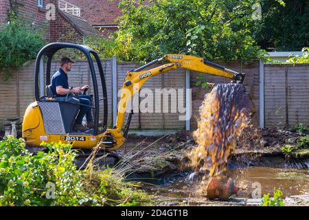 Gartenabräumarbeiten und Renovierungen, die im Oktober im Garten in Bournemouth, Dorset UK, stattfinden - Rodung des Gartenteiches mit jcb-Minibagger Stockfoto