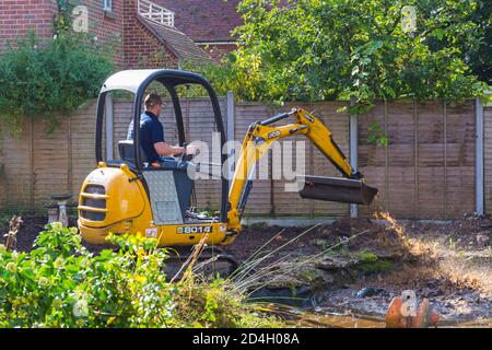 Gartenabräumarbeiten und Renovierungen, die im Oktober im Garten in Bournemouth, Dorset UK, stattfinden - Rodung des Gartenteiches mit jcb-Minibagger Stockfoto