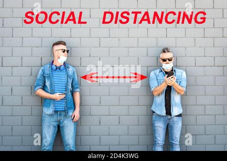 Zwei Freunde tragen abgesenkte Gesichtsschutzmasken mit Smart Mobile Telefone halten soziale Distanz, um COVID-19 Coronavirus-Krankheit zu verhindern - So Stockfoto