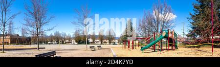 Leerer Schulhof an einem sonnigen Samstag. Polizei-Band um Spielplatz gewickelt, verhindern, dass Kinder mit Rutschen, Klettern Netz eine Schaukel Set. Stockfoto