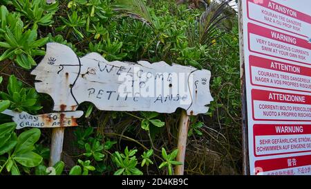 La Digue, Seychellen - 09/30/2018: Willkommen Zeichen des Strandes Petite Anse neben einem anderen Zeichen Warnung vor gefährlichen Strömungen in verschiedenen Sprachen. Stockfoto