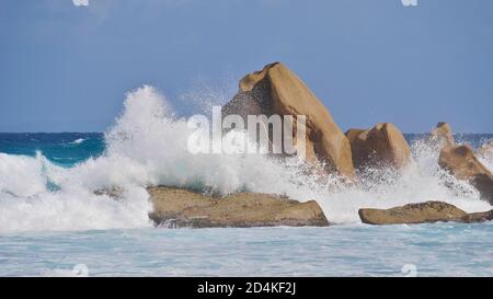 Riesige Wellen schlagen auf Granitfelsen mit hohen Sprühbrunnen am tropischen Grand Anse Strand im Süden der Insel La Digue, Seychellen. Stockfoto