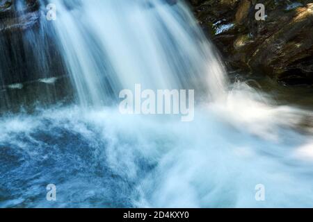 Kleiner Wasserfall in einem Bergbach zwischen Felsen, Wasserstrahlen sind in Bewegung verschwommen Stockfoto