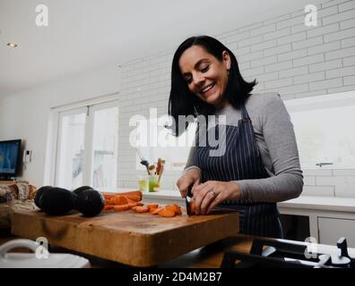 Junge Frau kocht in der Küche, hackt Gemüse, lächelt Stockfoto