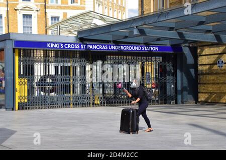 Eine Frau mit einer schützenden Gesichtsmaske und Gepäck geht vor einen geschlossenen Eingang des U-Bahnhofs King's Cross St Pancras, London, Großbritannien 17th. August 2020. Stockfoto