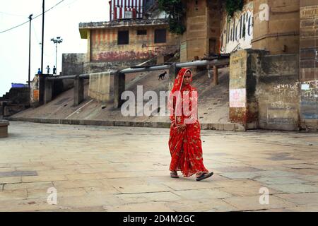 Eine Frau in rotem Kleid geht am Ganges Fluss in Varanasi, Ind Stockfoto