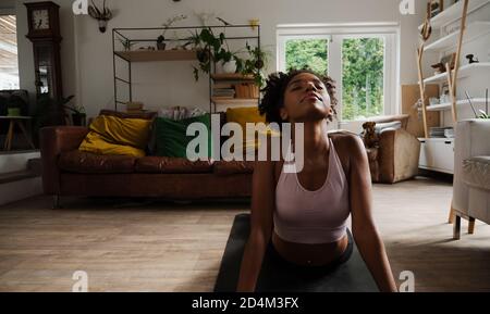 Schöne junge Frau, die von zu Hause aus arbeitet, nach oben streckt, Yoga in der Lounge Stockfoto
