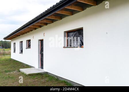 Eine neu aufgebrachte Schicht aus weißem Silikonputz an der Hauswand, Fenster und Tür sind mit schwarzer Folie gesichert. Stockfoto