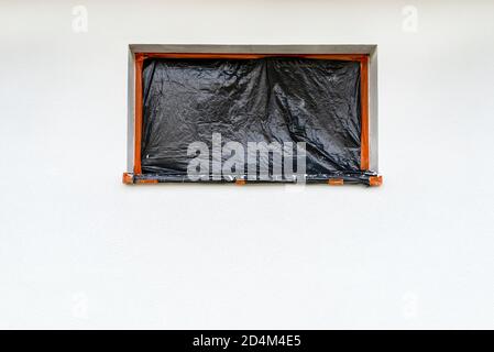 Eine neu aufgetragene Schicht aus weißem Silikonputz an der Hauswand, das Fenster ist mit schwarzer Folie gesichert. Stockfoto