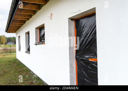 Eine neu aufgebrachte Schicht aus weißem Silikonputz an der Hauswand, Fenster und Tür sind mit schwarzer Folie gesichert. Stockfoto