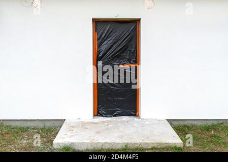 Eine neu aufgetragene Schicht aus weißem Silikonputz an der Hauswand, die Tür ist mit schwarzer Folie gesichert. Stockfoto