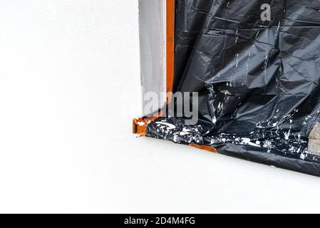 Eine neu aufgetragene Schicht aus weißem Silikonputz an der Hauswand, das Fenster ist mit schwarzer Folie gesichert. Stockfoto