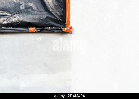 Eine neu aufgetragene Schicht aus weißem Silikonputz an der Hauswand, das Fenster ist mit schwarzer Folie gesichert. Stockfoto