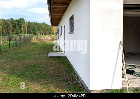 Eine neu aufgebrachte Schicht aus weißem Silikonputz an der Hauswand, Fenster und Tür sind mit schwarzer Folie gesichert. Stockfoto